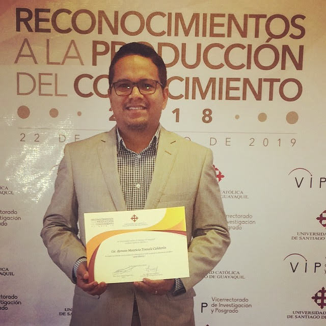 Byrone Tomalá con un diploma ante un panel de reconocimientos a la producción del conocimiento